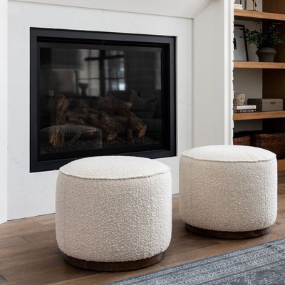 HANKI Ottomans collection — pair of round cream bouclé ottomans with wood bases by a fireplace